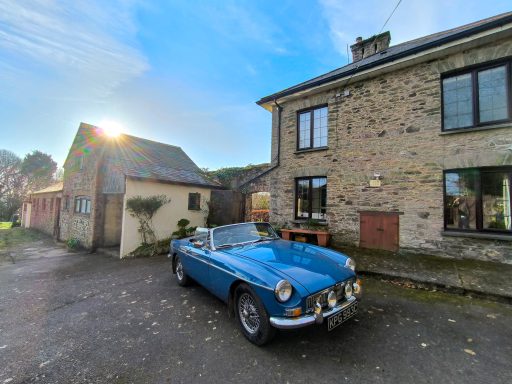 The rear of the house Classic blue convertible parked outside a stone house on a sunny day.
